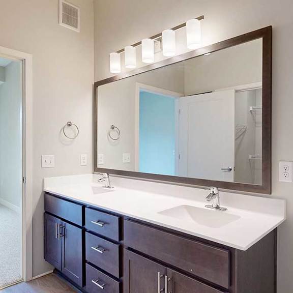 Thumbnail 21 of 29 A bathroom with a double sink marble vanity, oversized mirror, dark wooden cabinets, and a door open to a bedroom.
