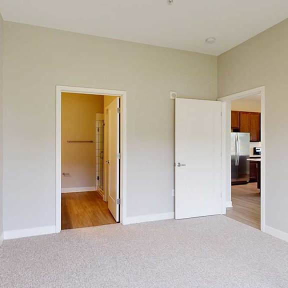 Thumbnail 17 of 29 A carpeted bedroom with an attached bathroom and a door open to the living room.