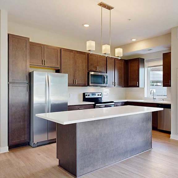 Thumbnail 11 of 29 A kitchen with dark wood cabinets, quartz countertops, a large island, stainless steel appliances, and a designer backsplash.