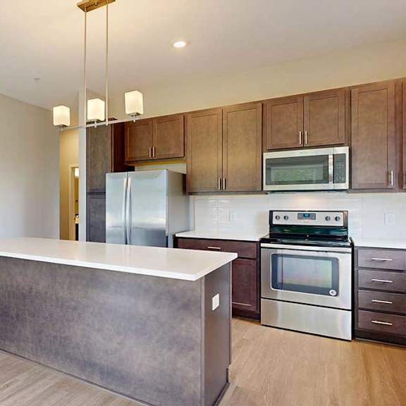 Thumbnail 14 of 29 A kitchen with dark wood cabinets, quartz countertops, a large island, stainless steel appliances, and a designer backsplash.