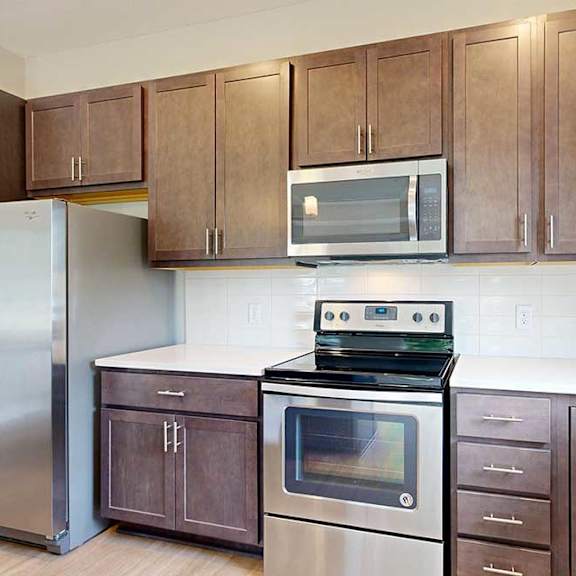 Thumbnail 13 of 29 A kitchen with dark wood cabinets, quartz countertops, stainless steel appliances, and a designer backsplash.