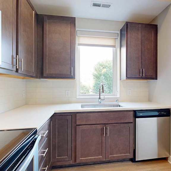 Thumbnail 12 of 29 A kitchen with dark wooden cabinets, quartz countertops, a tile backsplash, an island, and a window over the kitchen sink.