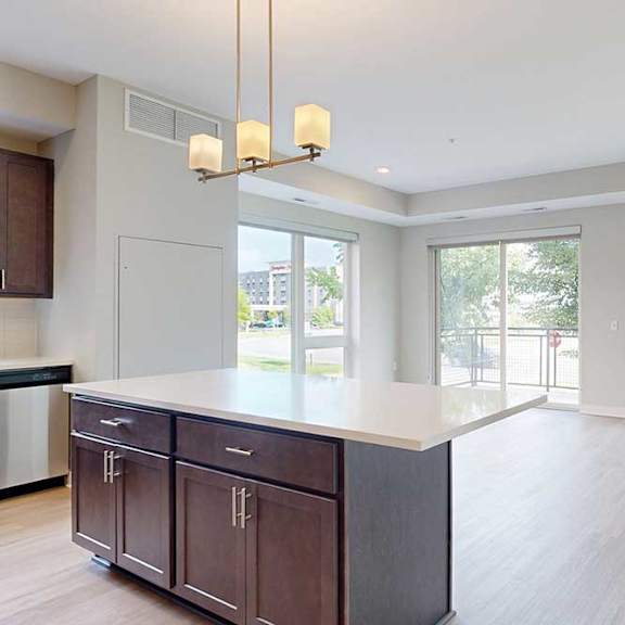 Thumbnail 7 of 29 A kitchen with dark wooden cabinets and a large island, in front of a spacious living room.