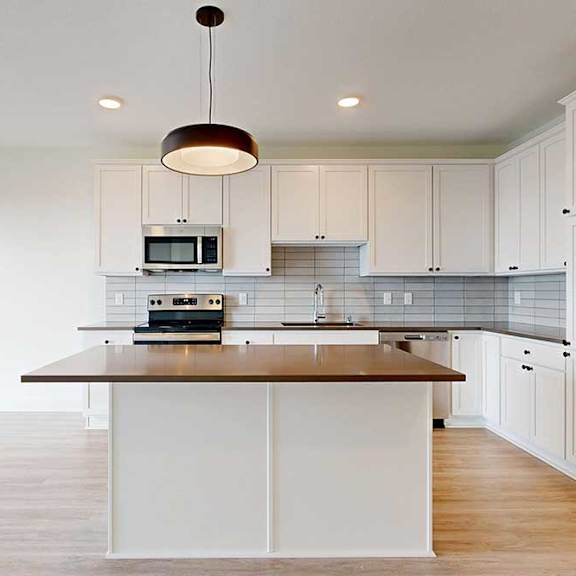 Thumbnail 10 of 18 Modern kitchen with sleek white cabinets, stainless steel appliances, and light wood flooring. Central island with a black countertop under a stylish pendant light.