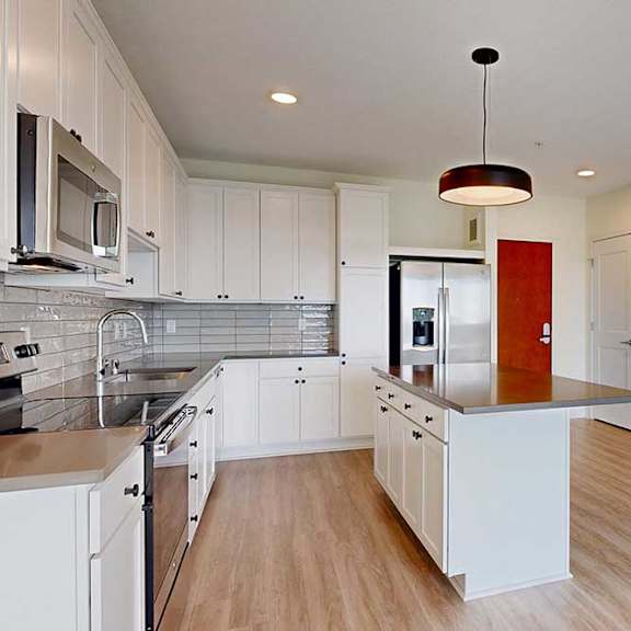 Thumbnail 8 of 18 Modern kitchen with white cabinets, stainless steel appliances, and a central island under a dark pendant light. Light wood floor adds warmth.