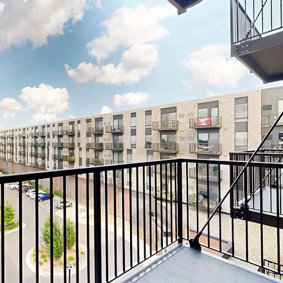 Thumbnail 11 of 17 A balcony overlooks a parking lot and apartment building