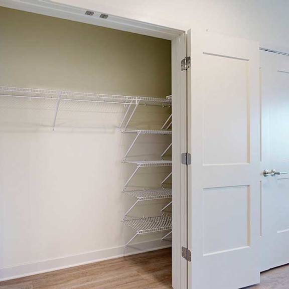 Thumbnail 6 of 17 Open closet with white double doors, featuring empty white wire shelves on the right and a light beige interior