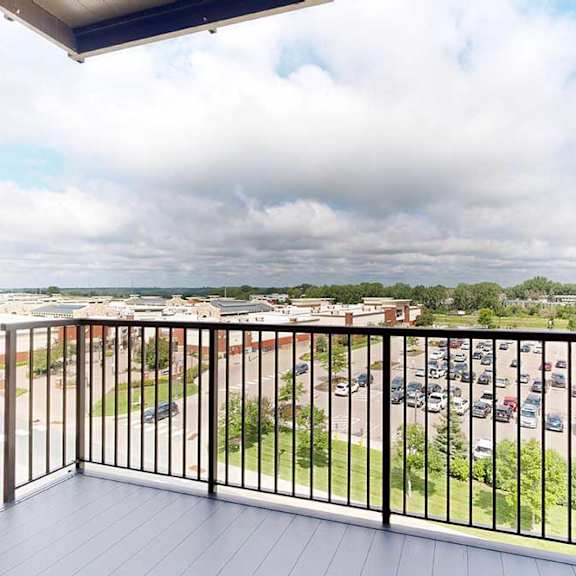 Thumbnail 10 of 23 A balcony with a black railing overlooks a parking lot and greenery.