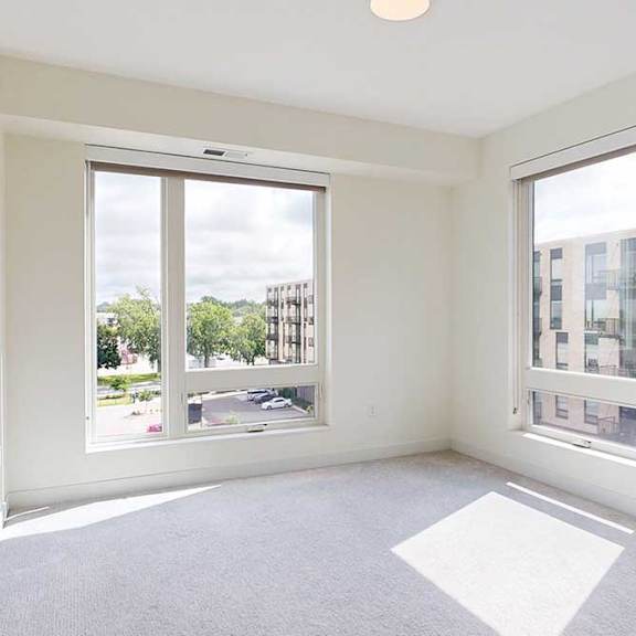 Thumbnail 19 of 23 Bright, empty room with large windows, soft ,showcasing natural light and a view of neighboring buildings.