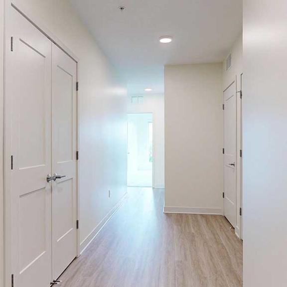 Thumbnail 2 of 23 A long hallway with white doors and wood floors.