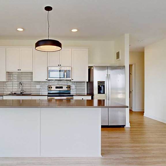 Thumbnail 12 of 23 Modern kitchen featuring white cabinets, stainless steel appliances, and a spacious island with a sleek countertop and pendant lighting.
