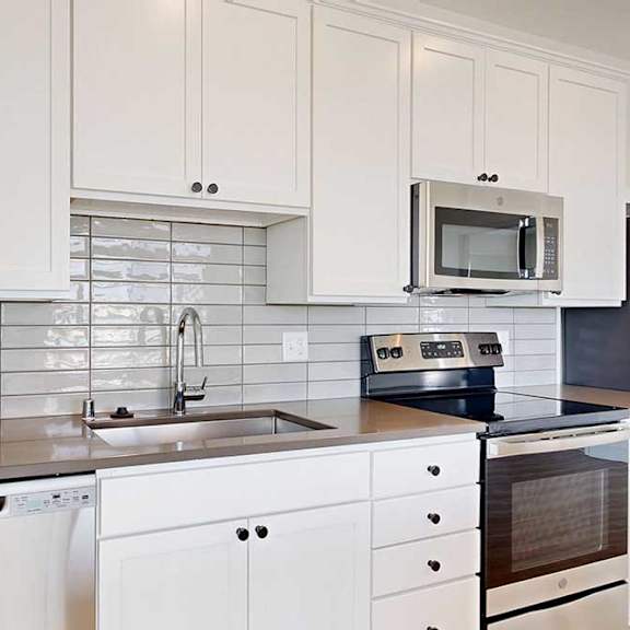 Thumbnail 7 of 23 Modern kitchen with white cabinets, gray tile backsplash, stainless steel sink, dishwasher, and appliances.