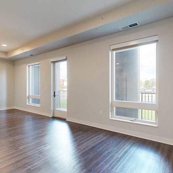 Thumbnail 8 of 31 A spacious, modern living room with dark hardwood floors and light walls. Three large windows and a glass door let in natural light, creating an open, airy feel.