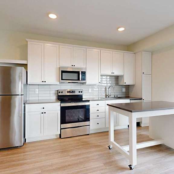 Thumbnail 13 of 19 Bright, modern kitchen with white cabinets, a movable island, and light wood flooring. Large glass doors open to a balcony with a scenic view.