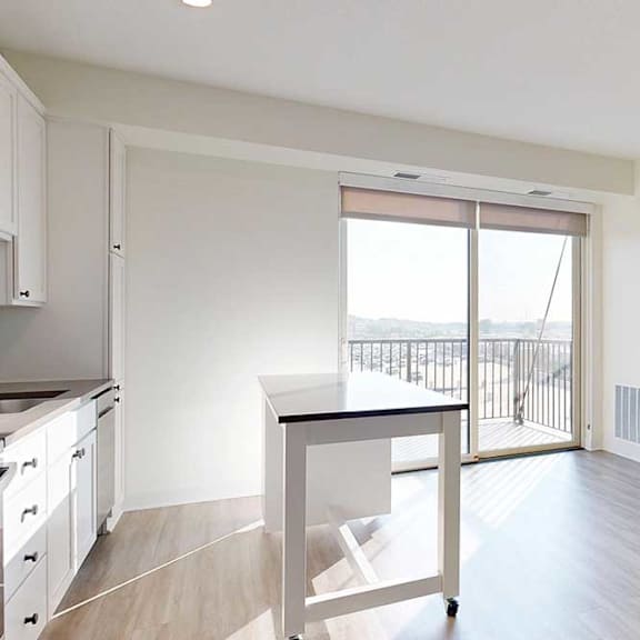 Thumbnail 6 of 19 Bright, modern kitchen with light wood flooring, white cabinets, and a central island. Large glass doors lead to a balcony, creating an airy feel.