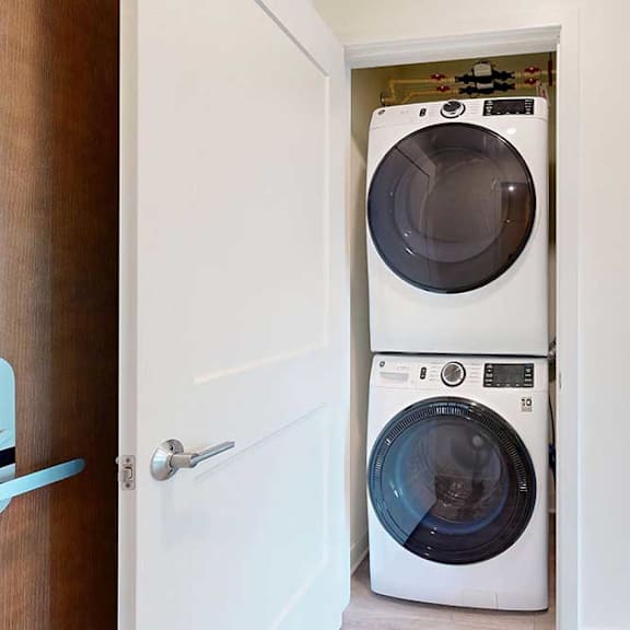 Thumbnail 16 of 19 Stacked front-loading washer and dryer in a small laundry closet. The space is neatly organized, with white doors open