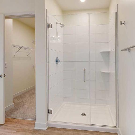 Thumbnail 24 of 26 Modern bathroom with a glass-enclosed shower featuring white tiles, chrome fixtures, and a metal towel bar. Open door reveals a carpeted walk-in closet.
