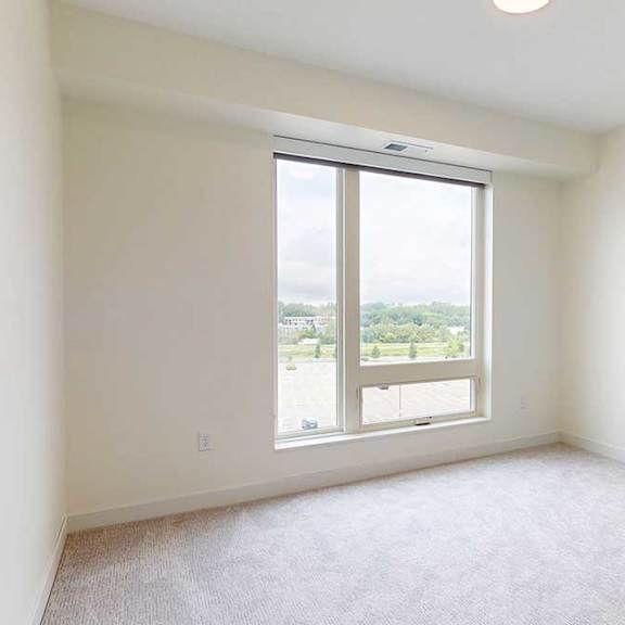Thumbnail 7 of 26 A large, empty bedroom with a window overlooking a parking lot.