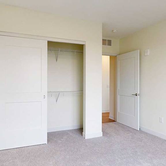 Thumbnail 8 of 26 A white closet door is open in a bedroom with carpeted floor.