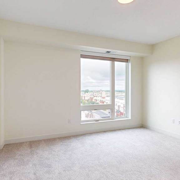 Thumbnail 20 of 26 A large empty bedroom with a window overlooking a cityscape.