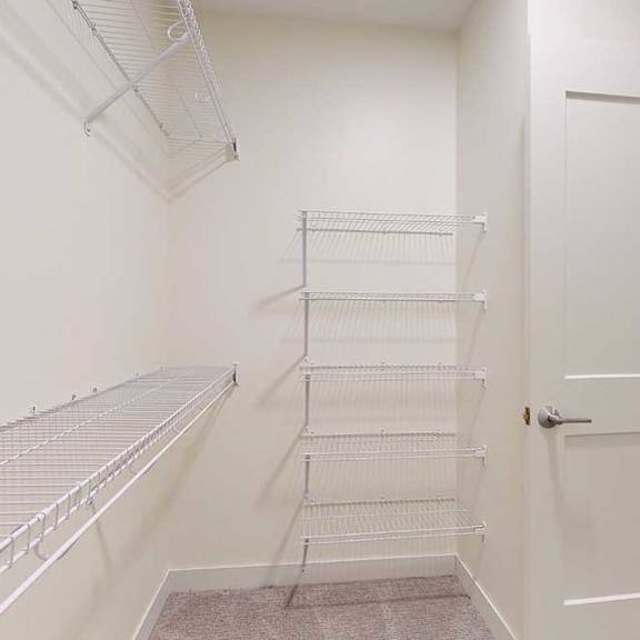 Thumbnail 26 of 26 Empty walk-in closet with beige walls and white wire shelving on the left and back walls. A partially open white door is visible