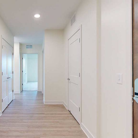 Thumbnail 2 of 26 A long hallway with white walls and wood floors.
