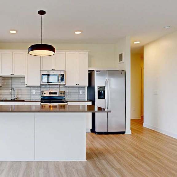 Thumbnail 11 of 26 A modern kitchen with white cabinets and a wooden floor.