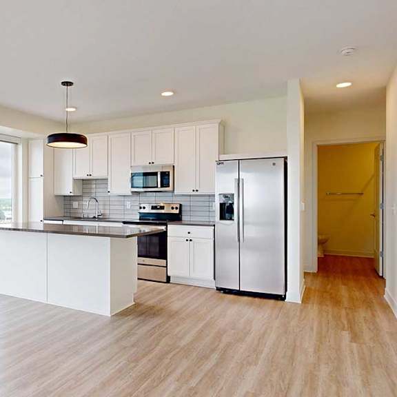 Thumbnail 18 of 26 Modern, bright kitchen with light wood flooring, white cabinets, and stainless steel appliances. Large windows and a small balcony offer an open view.