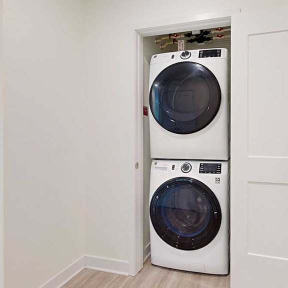Thumbnail 3 of 26 Stacked washer and dryer in a small closet with an open white door, placed on light wooden flooring.