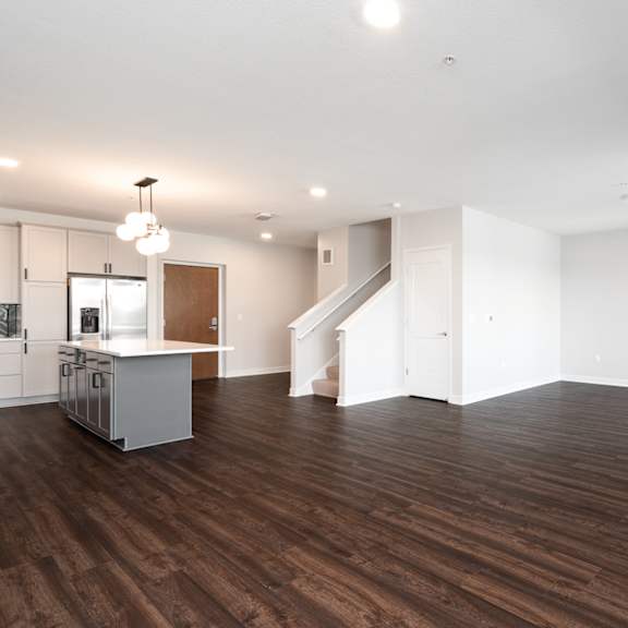 Thumbnail 4 of 15 large open living and dining area with dark hardwood flooring. Kitchen counter and staircase to the left.