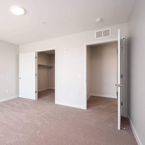 Thumbnail 9 of 15 large bedroom with beige carpet and white walls. Two open doors, one leading to the walk in closet and the other leads to the rest of the apartment.