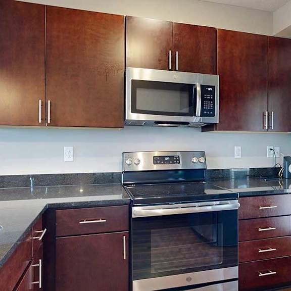 Thumbnail 13 of 25 A kitchen with dark drown cabinets, granite countertops, and a stainless steel microwave and range.