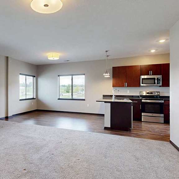 Thumbnail 8 of 25 A carpeted living room with several windows, open to a dining room and kitchen with hardwood-style flooring.