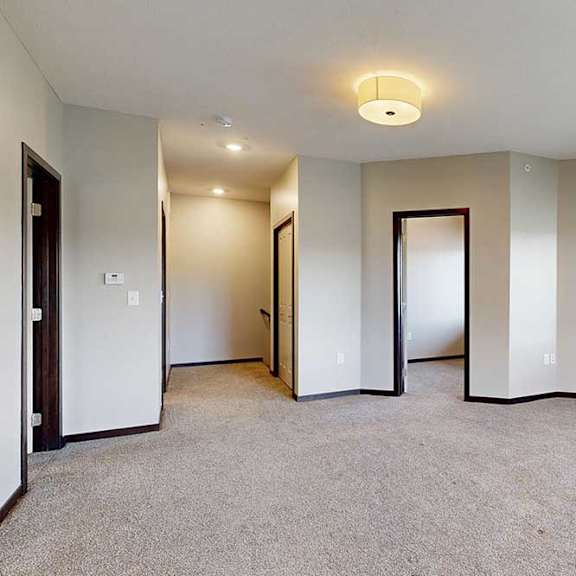 Thumbnail 17 of 25 A spacious carpeted living room with an electric fireplace and an open door to a den space.