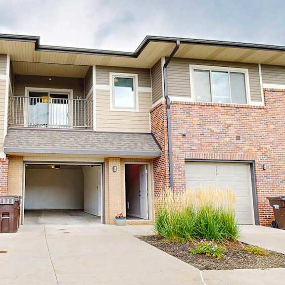 a two-story apartment building with an attached garage on the first floor, and a balcony above it.