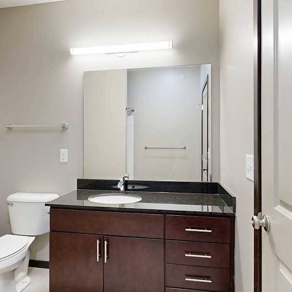 Thumbnail 23 of 24 A bathroom with a granite vanity, dark wooden cabinets, and an oversized mirror with overhead lighting.