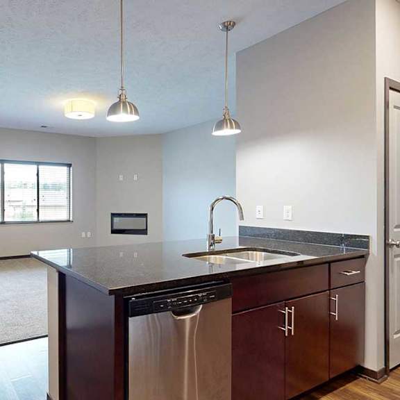 Thumbnail 11 of 24 A kitchen peninsula with a double basin sink in front of a carpeted living room.