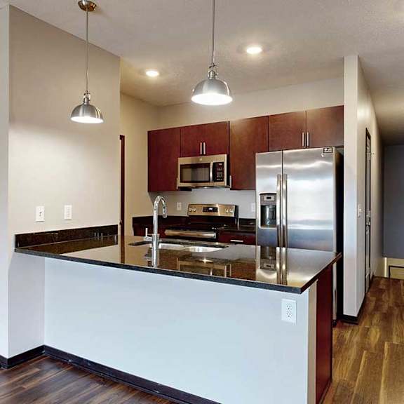Thumbnail 7 of 24 A galley kitchen with dark granite countertops, dark wooden cabinets, and stainless steel appliances.