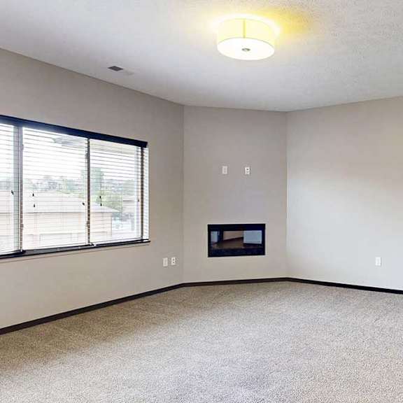 Thumbnail 14 of 24 A carpeted living room with an electric fireplace and a large window.
