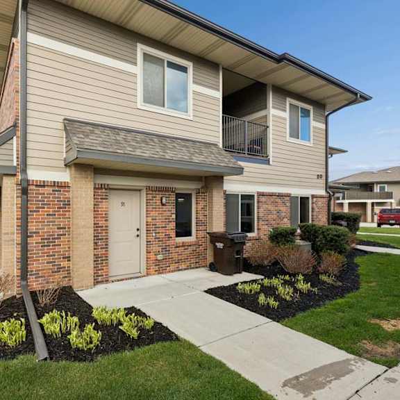 Thumbnail 3 of 14 Exterior view of a modern apartment community building with stone and brick accents, covered entryways, and landscaped grounds.