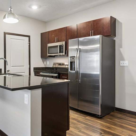 Thumbnail 6 of 14 Modern apartment kitchen with stainless steel appliances, dark cabinetry, pendant lighting, and a breakfast bar island.