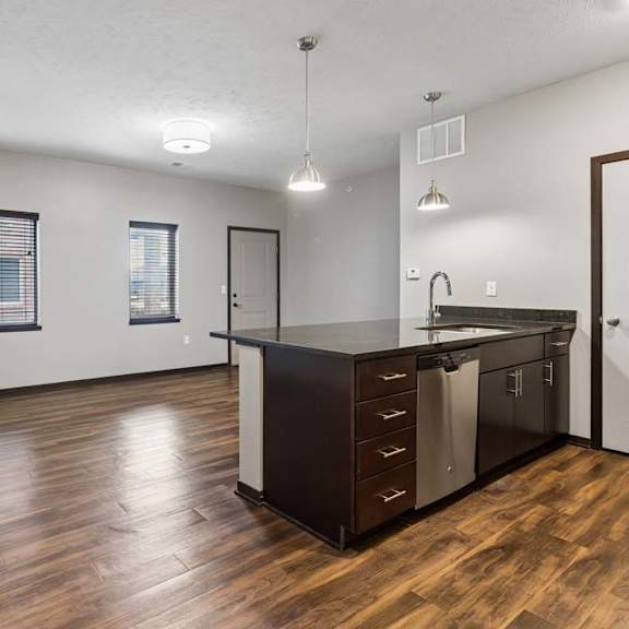 Thumbnail 8 of 14 Open-concept apartment living area with wood-style flooring, large windows, and a kitchen featuring a central island.