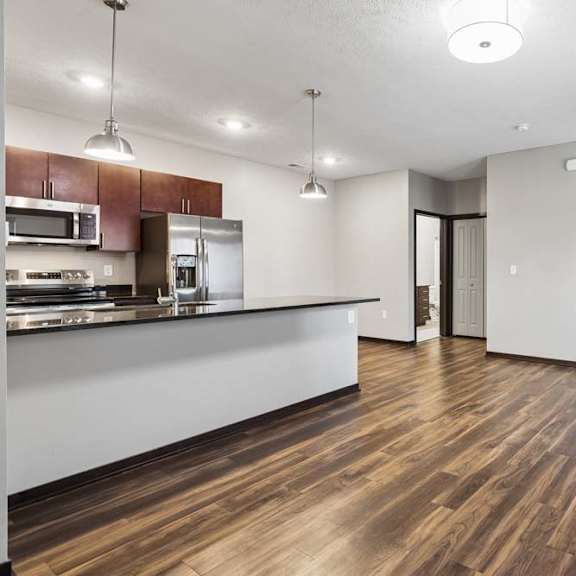 Thumbnail 4 of 14 Open living and dining area with wood-style flooring, breakfast bar seating, and a seamless apartment floor plan.