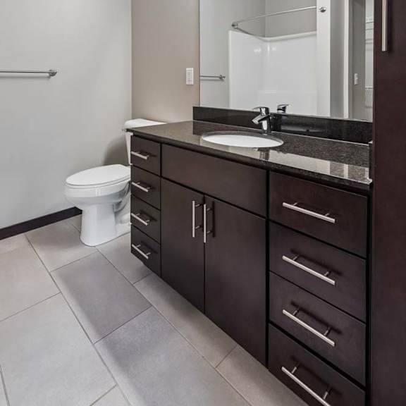 Thumbnail 12 of 18 Apartment bathroom featuring a dark wood vanity, large mirror, and bright neutral finishes.