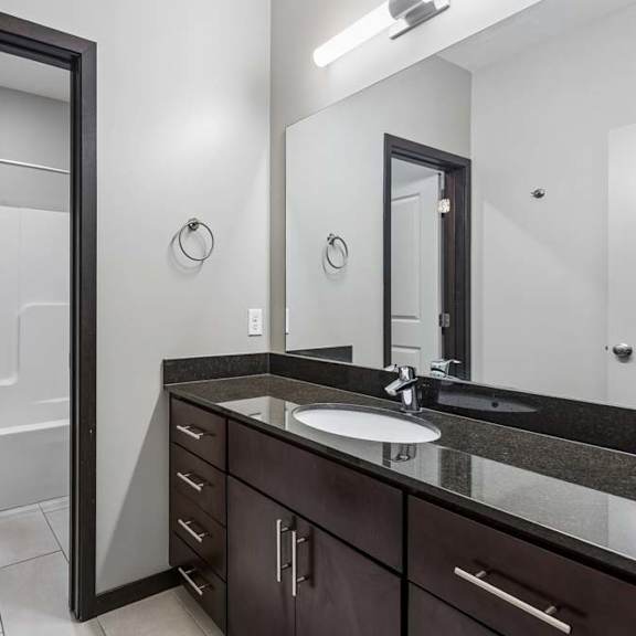 Thumbnail 17 of 18 Bathroom with dark wood vanity, solid-surface countertop, framed mirror, and tub-shower combination.