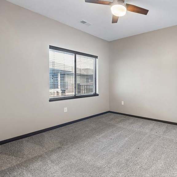 Thumbnail 13 of 18 Spacious bedroom with large window, gray carpet, ceiling fan, and neutral finishes throughout.