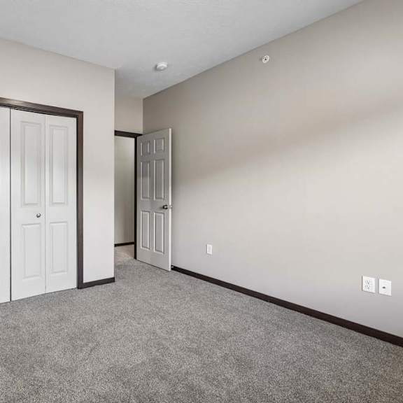 Thumbnail 14 of 18 Bedroom with gray carpet, neutral walls, and double-door closet in a bright apartment interior.