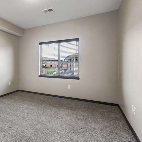 Thumbnail 15 of 18 Bright bedroom with gray carpet, neutral walls, and a large window overlooking the apartment community.