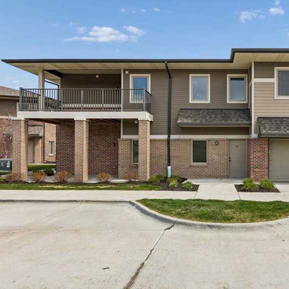 Thumbnail 3 of 18 Townhome-style apartment exterior with attached garages, brick accents, and landscaped front entry.