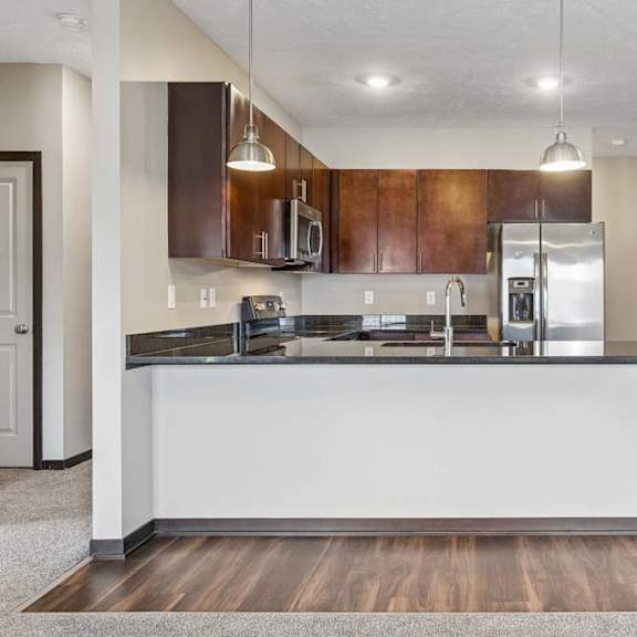 Thumbnail 7 of 18 Modern kitchen with dark wood cabinetry, stainless steel appliances, peninsula seating, and wood-look flooring.